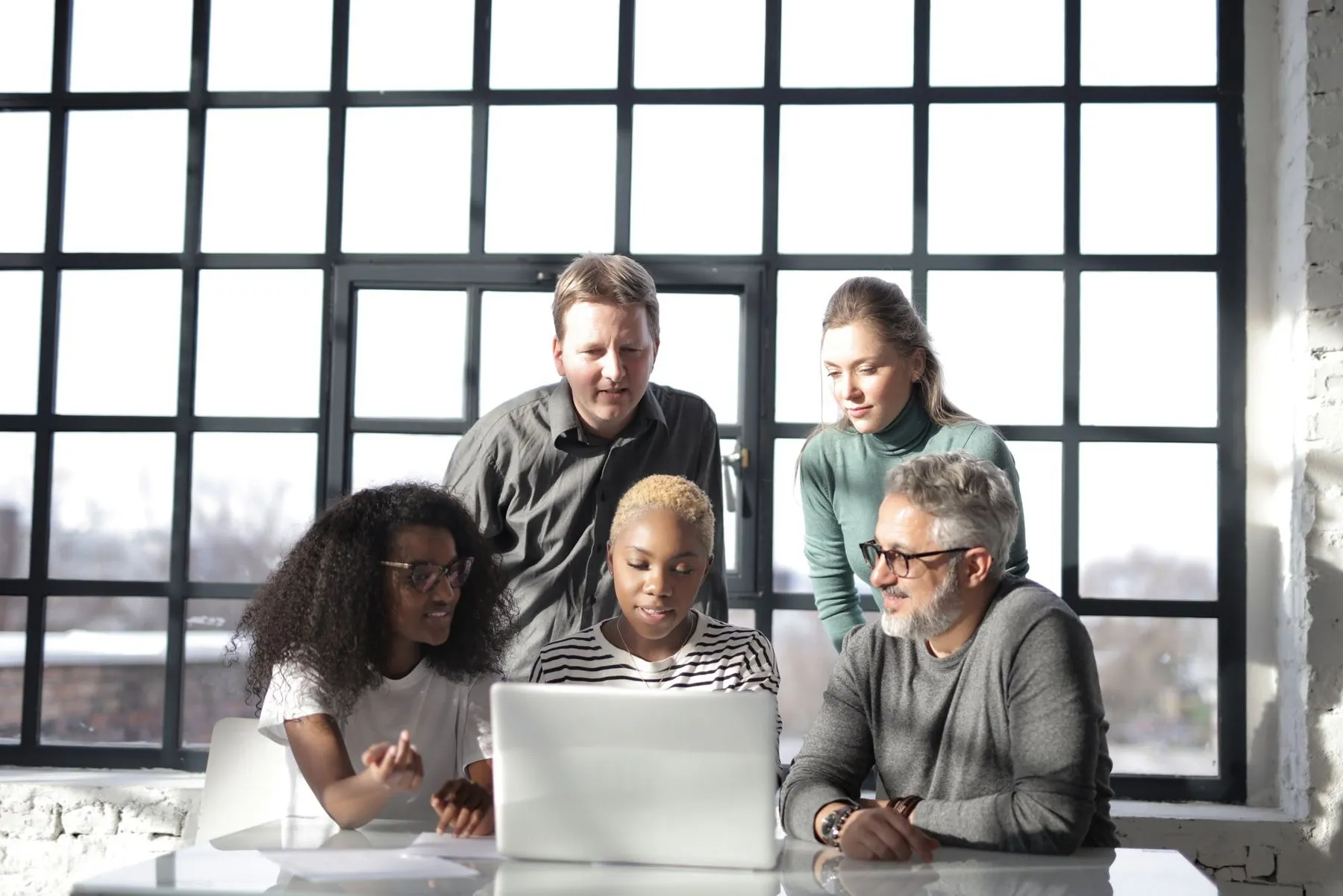 Colleagues collaborating around a laptop by a large window